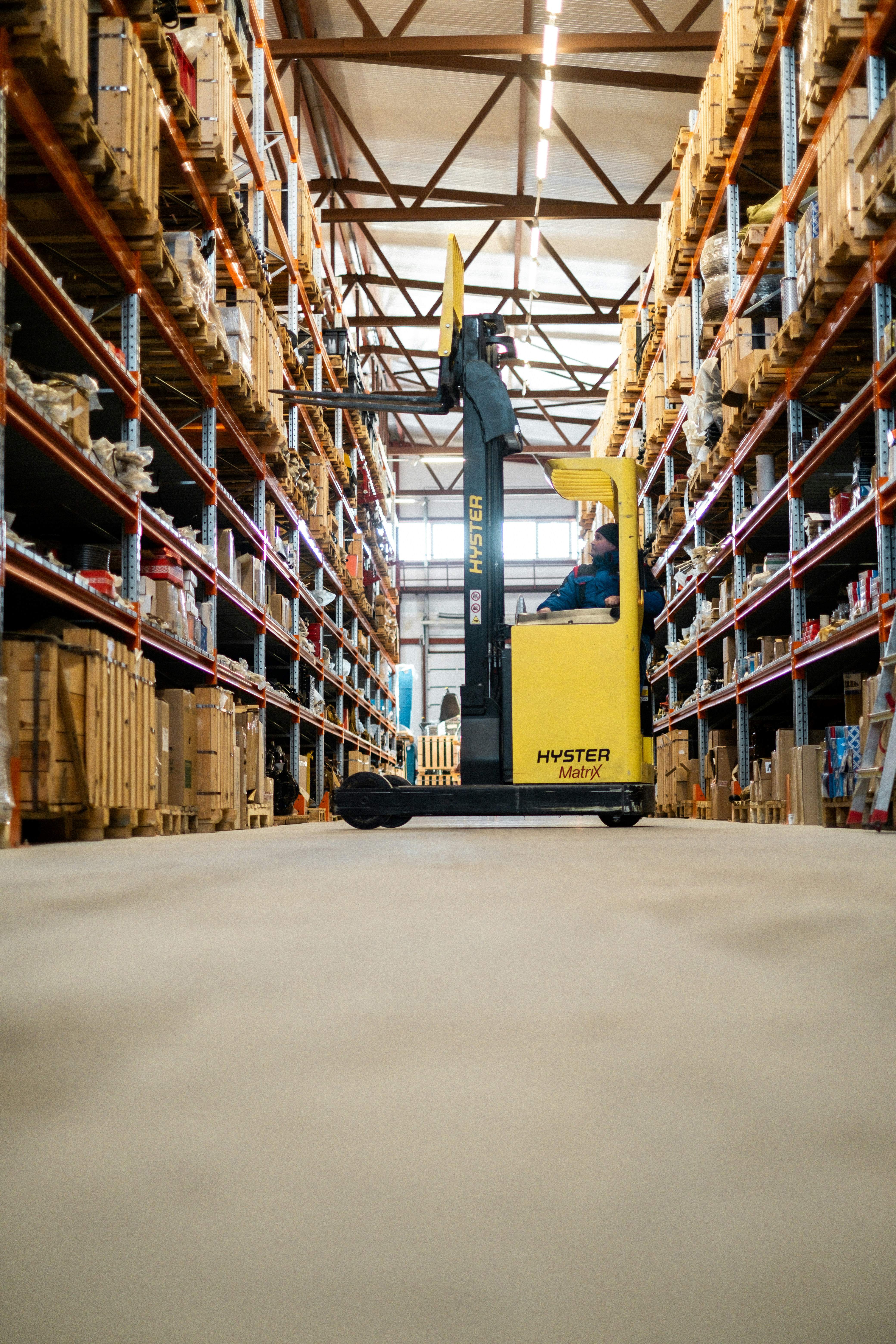 Forklift operating in a warehouse aisle lined with tall storage racks